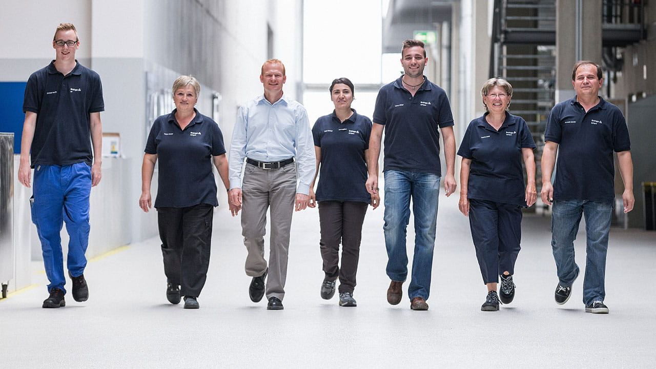 7 trabajadores de Ensinger caminan en fila hacia observadores en una nave de producción